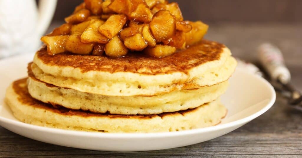 stack of three pancakes on plate with apple topping