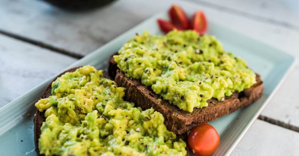 two slices of avocado toast on a plate with tomatoes