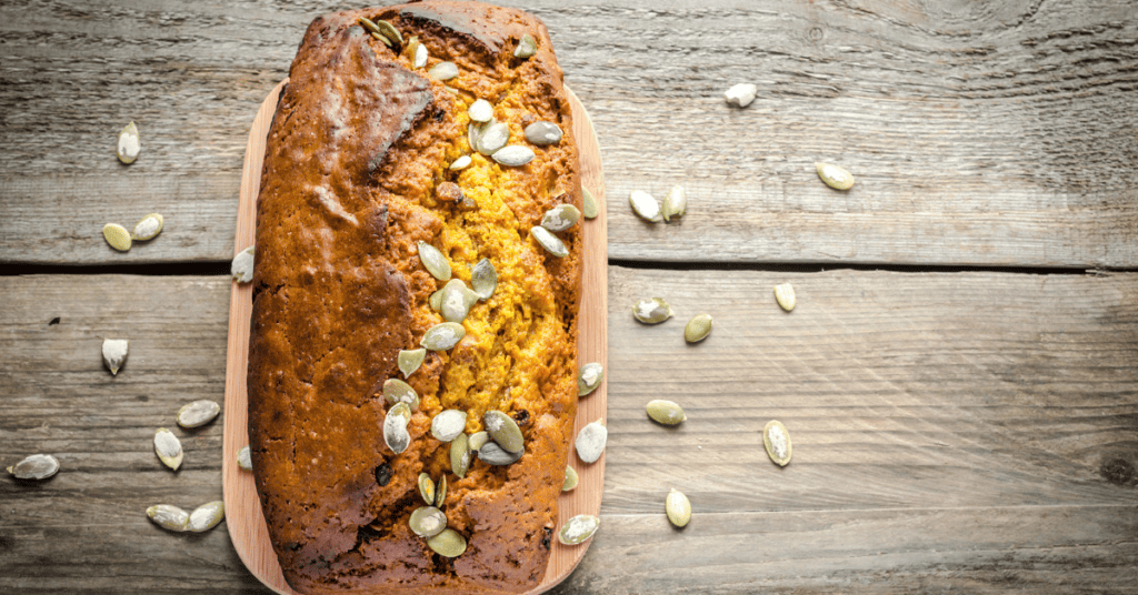 loaf of pumpkin bread on wooden counter with pumpkin seeds sprinkled on top and on counter