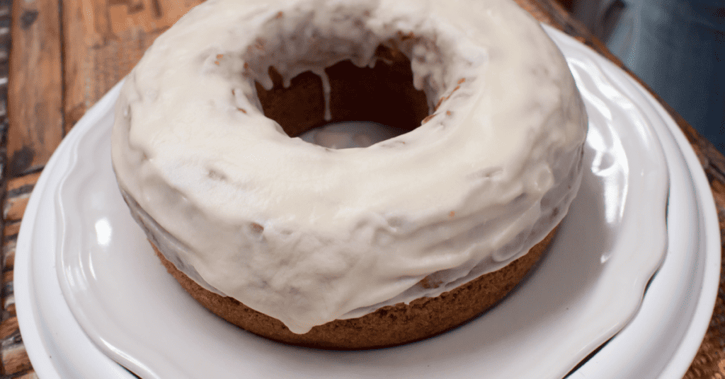 pumpkin donut with white frosting on white plate on wooden surface