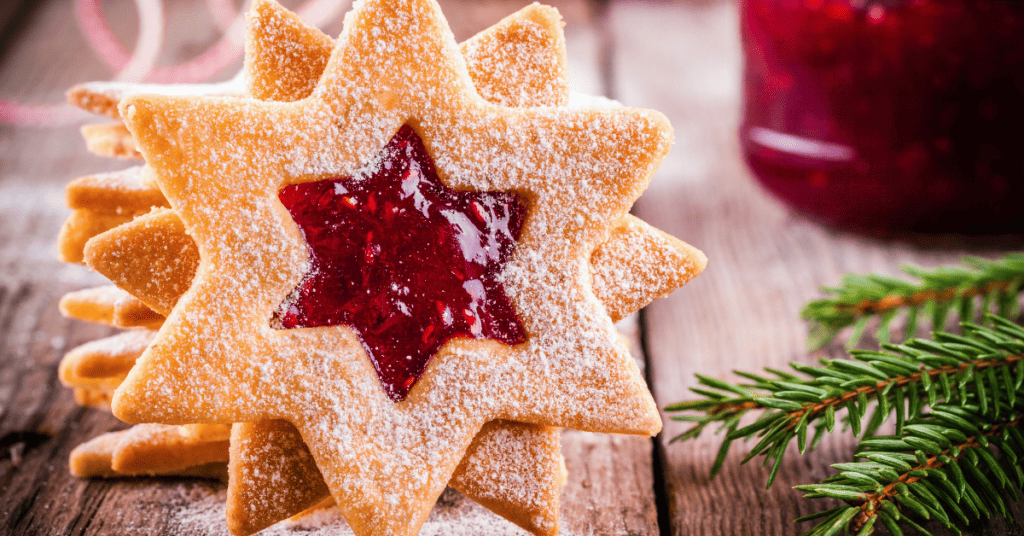 star shaped raspberry linzer cookies  on wooden counter with jam and pine needles to the right