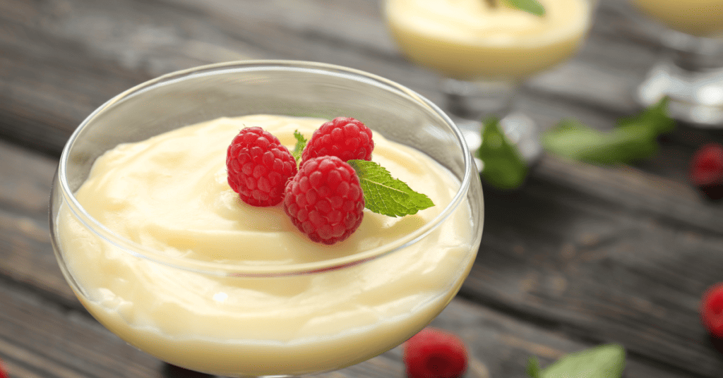 vanilla pudding in glass dish with raspberries on top